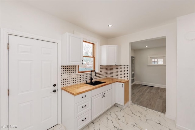 kitchen featuring butcher block counters, a sink, white cabinets, and tasteful backsplash