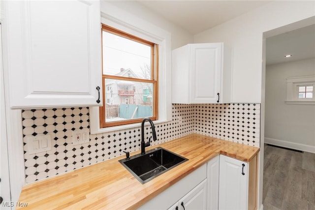 kitchen with butcher block countertops, a sink, white cabinetry, and decorative backsplash