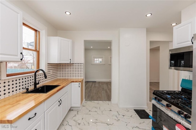 kitchen with marble finish floor, butcher block counters, appliances with stainless steel finishes, a healthy amount of sunlight, and a sink