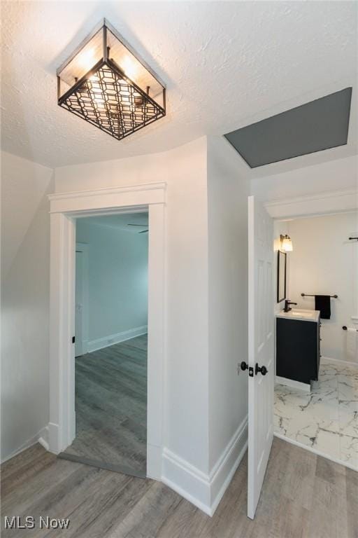 hall with light wood-style flooring, baseboards, and a textured ceiling