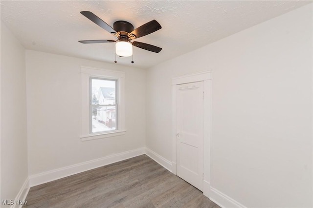 empty room with a textured ceiling, ceiling fan, wood finished floors, and baseboards