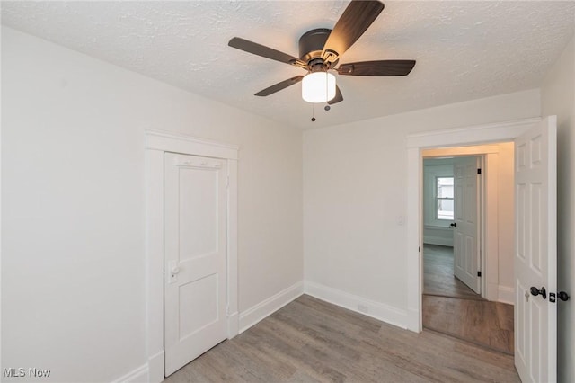 empty room featuring a ceiling fan, baseboards, light wood-style flooring, and a textured ceiling