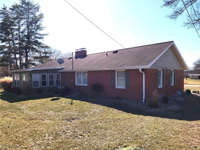 back of property featuring brick siding, a lawn, a chimney, and central AC unit