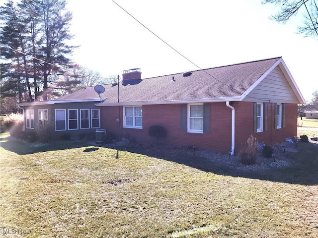 back of property with brick siding, a lawn, a chimney, and a shingled roof