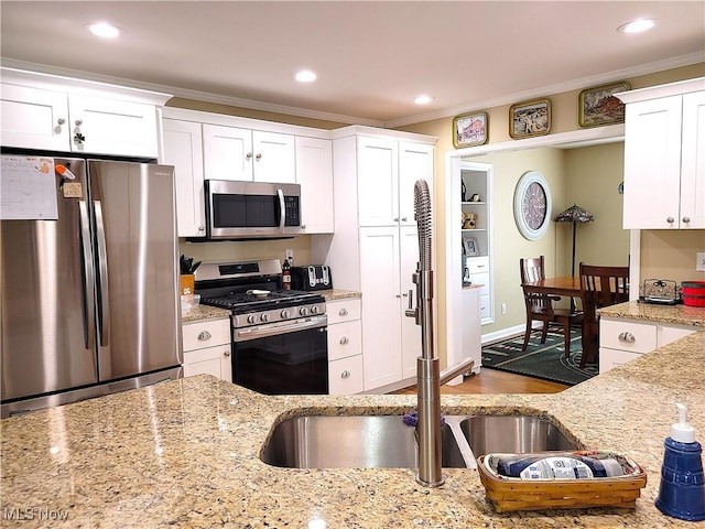 kitchen with stainless steel appliances, ornamental molding, light stone countertops, and white cabinets