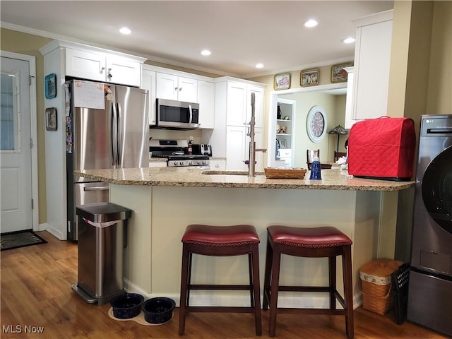 kitchen with stainless steel appliances, dark wood-type flooring, a kitchen bar, and light stone countertops