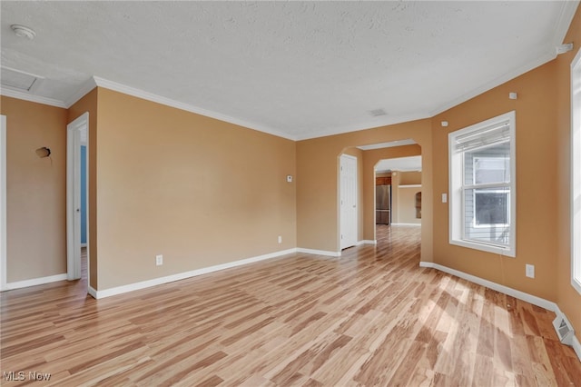 empty room with light wood-style floors, baseboards, arched walkways, and crown molding
