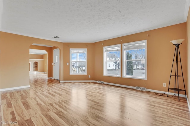 empty room with arched walkways, visible vents, a textured ceiling, and light wood finished floors