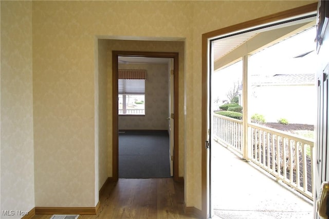 corridor with wood finished floors, baseboards, and wallpapered walls