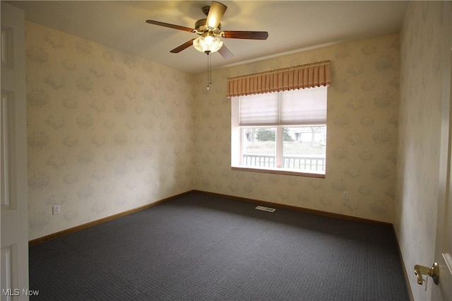 carpeted empty room with wallpapered walls, baseboards, visible vents, and a ceiling fan