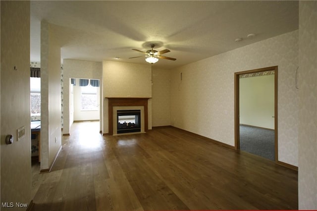 unfurnished living room featuring a ceiling fan, wood finished floors, a multi sided fireplace, and wallpapered walls