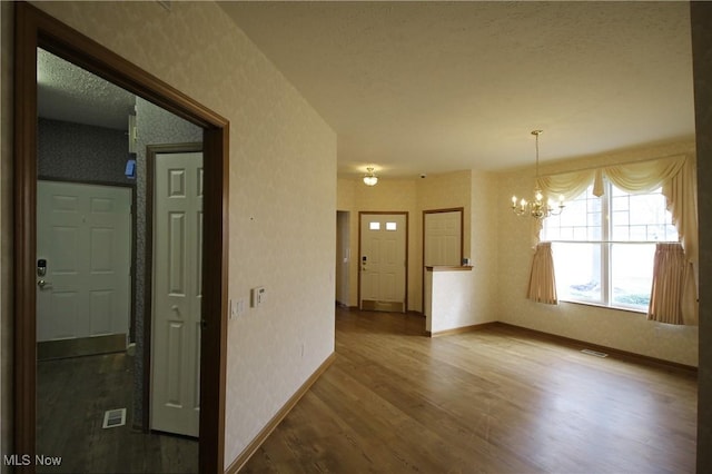 interior space featuring wallpapered walls, visible vents, baseboards, wood finished floors, and a chandelier