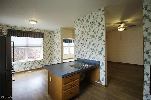 kitchen featuring dark wood-type flooring, brown cabinets, black appliances, dark countertops, and wallpapered walls