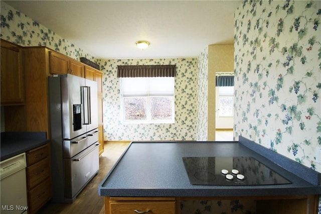 kitchen featuring high quality fridge, dishwasher, brown cabinetry, dark countertops, and wallpapered walls