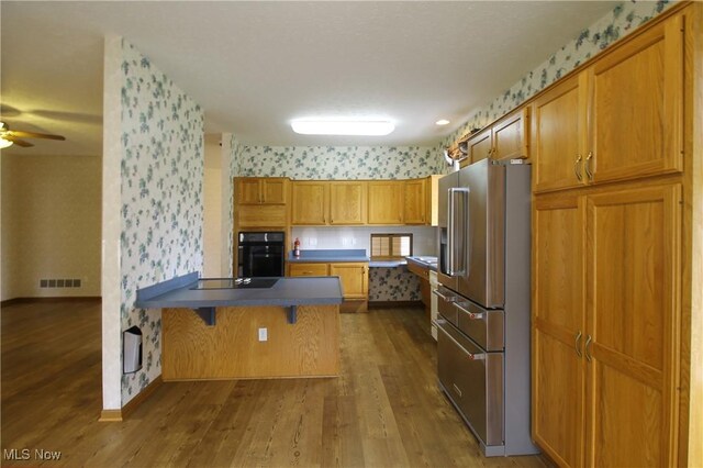 kitchen featuring visible vents, a peninsula, black appliances, and wallpapered walls