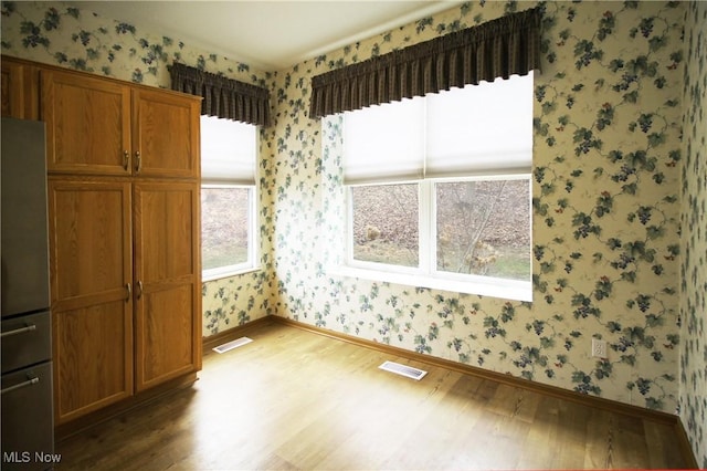 spare room with wallpapered walls, baseboards, visible vents, and wood finished floors