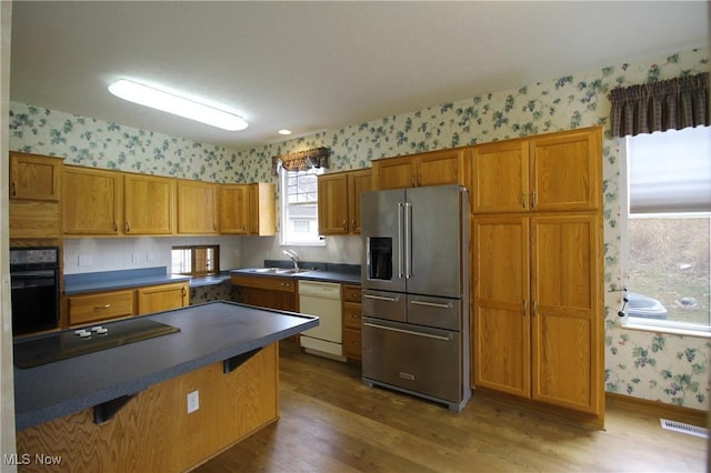 kitchen with wallpapered walls, visible vents, dark countertops, brown cabinets, and black appliances