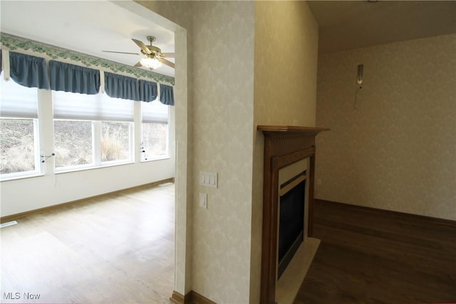 living room with a fireplace, ceiling fan, wood finished floors, baseboards, and wallpapered walls