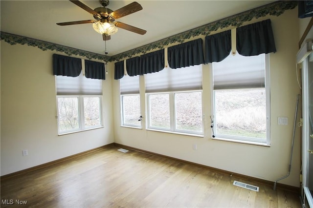 empty room with ceiling fan, wood finished floors, visible vents, and baseboards