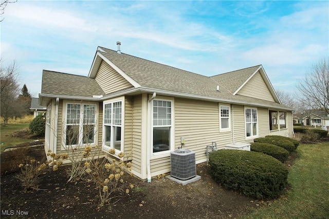 back of house with central air condition unit and a shingled roof