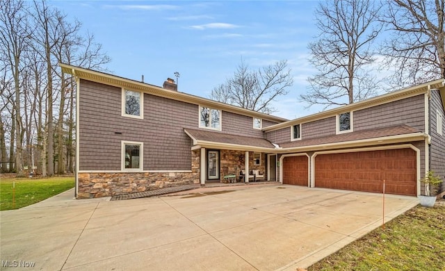 view of front facade with an attached garage, stone siding, a chimney, and concrete driveway