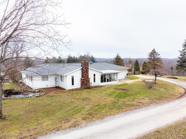 view of front facade featuring a front lawn, a chimney, driveway, and a shingled roof