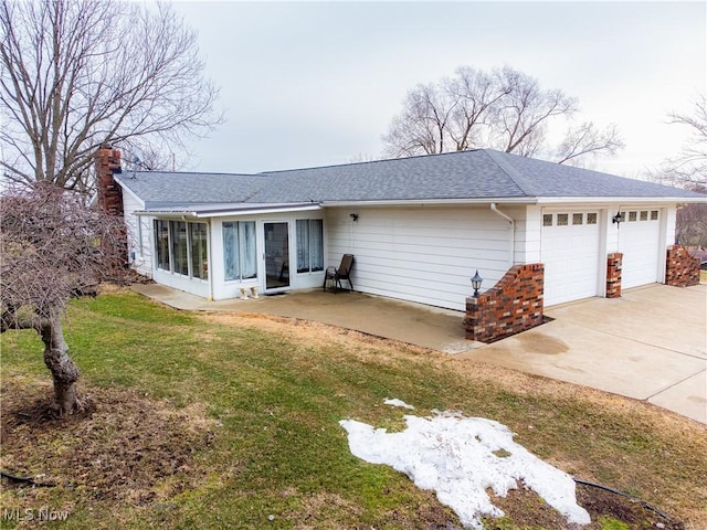 back of property with roof with shingles, driveway, an attached garage, a yard, and a chimney