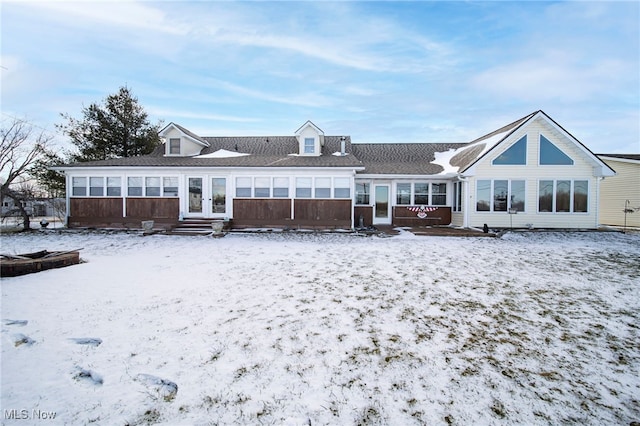 snow covered rear of property featuring french doors and a sunroom