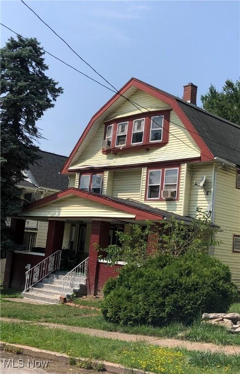 view of front of property featuring cooling unit, covered porch, a gambrel roof, and a chimney