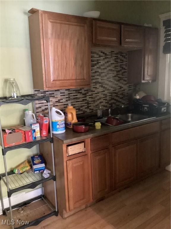 kitchen with decorative backsplash, dark countertops, light wood-type flooring, and a sink