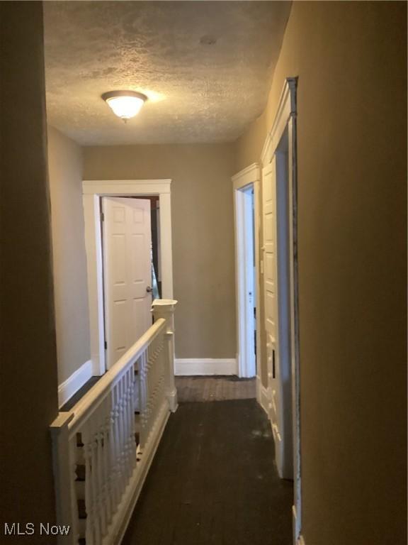 hall featuring baseboards, dark wood-style flooring, and a textured ceiling