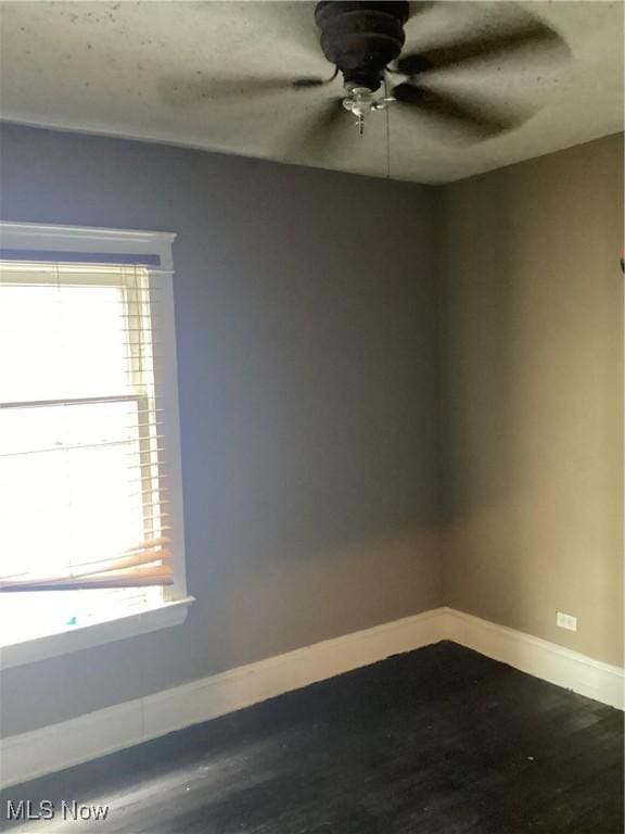 spare room with dark wood-style floors, a ceiling fan, and baseboards