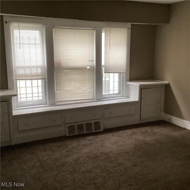 empty room featuring a wealth of natural light, baseboards, visible vents, and dark colored carpet