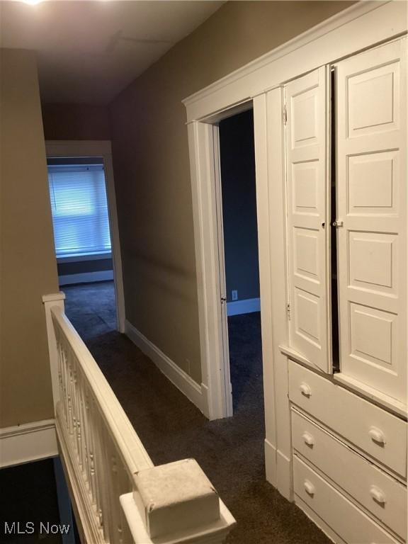 hallway with an upstairs landing, baseboards, and dark carpet