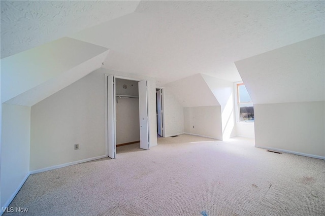 additional living space featuring vaulted ceiling, carpet flooring, baseboards, and a textured ceiling