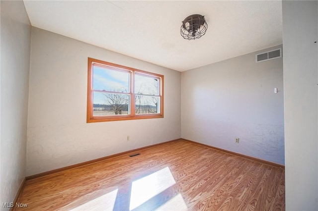 empty room with wood finished floors, visible vents, and baseboards