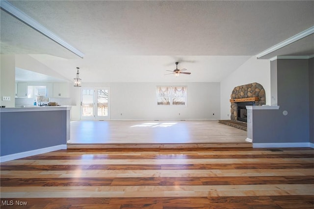 unfurnished living room featuring baseboards, a stone fireplace, wood finished floors, and a ceiling fan