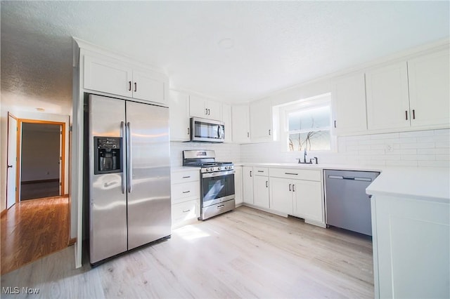 kitchen featuring decorative backsplash, appliances with stainless steel finishes, white cabinets, and light wood finished floors