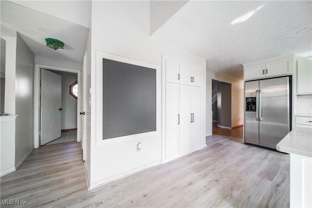 kitchen with light wood-type flooring, light countertops, a textured ceiling, white cabinetry, and stainless steel fridge