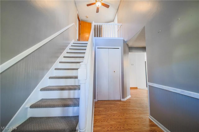 stairway featuring ceiling fan, a wainscoted wall, and wood finished floors