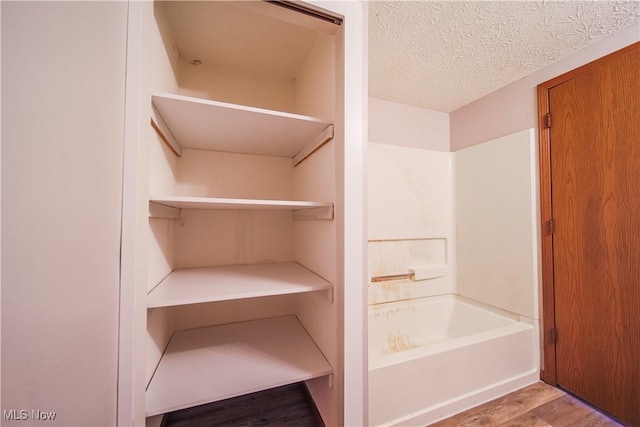 full bathroom featuring a textured ceiling, wood finished floors, and bathing tub / shower combination