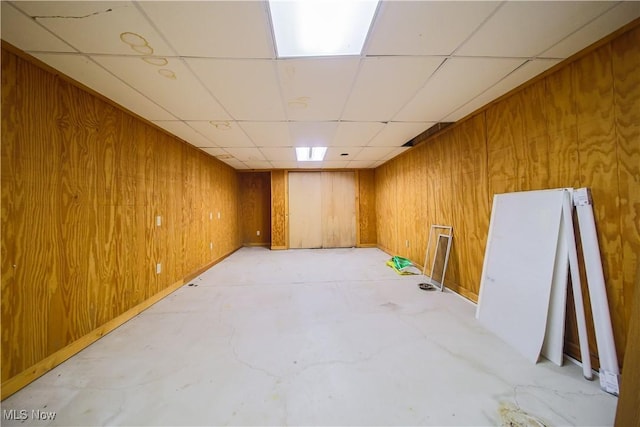 unfurnished room featuring a paneled ceiling, concrete flooring, and wood walls