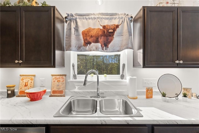 kitchen with dark brown cabinetry, stainless steel dishwasher, light stone counters, and a sink