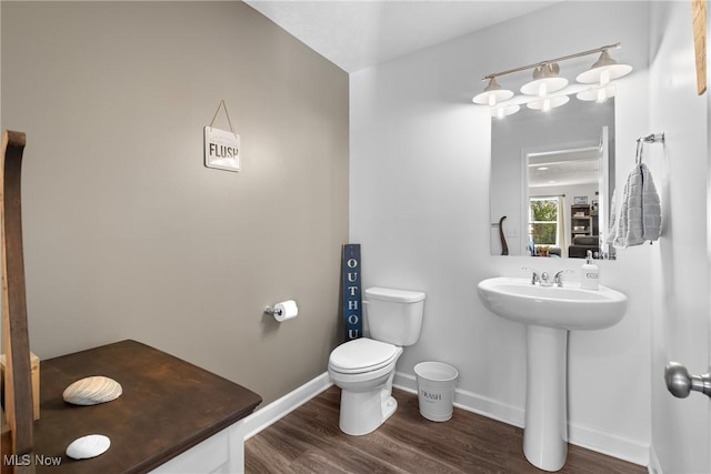 half bathroom featuring toilet, wood finished floors, baseboards, and a sink