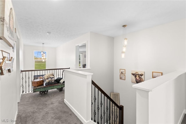 corridor featuring baseboards, a textured ceiling, carpet flooring, an upstairs landing, and a chandelier