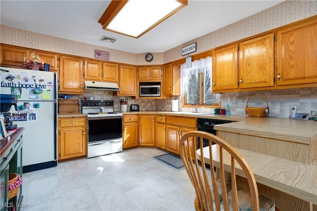 kitchen with white appliances, range hood, brown cabinetry, wallpapered walls, and light countertops