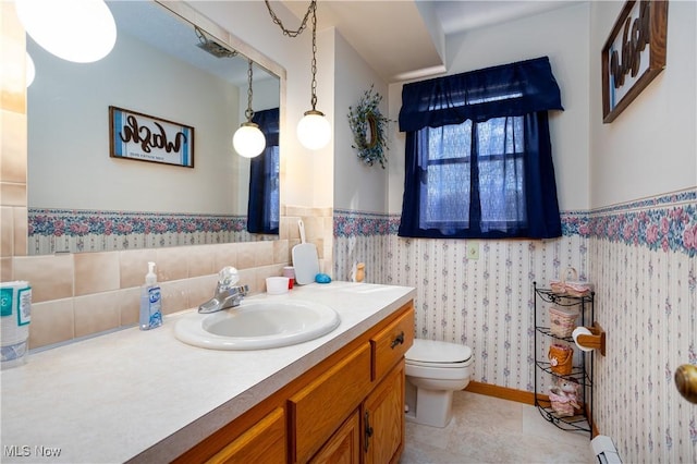 half bathroom with tile patterned floors, toilet, wainscoting, wallpapered walls, and vanity