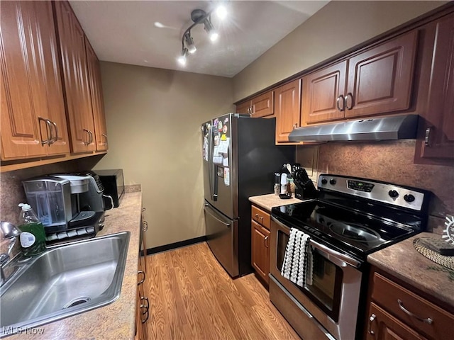 kitchen with backsplash, under cabinet range hood, light wood-style floors, stainless steel appliances, and a sink