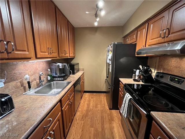 kitchen featuring light wood-style flooring, under cabinet range hood, a sink, stainless steel appliances, and decorative backsplash