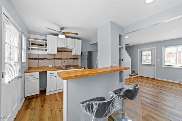 kitchen featuring butcher block counters, light wood-style flooring, freestanding refrigerator, white cabinets, and a sink